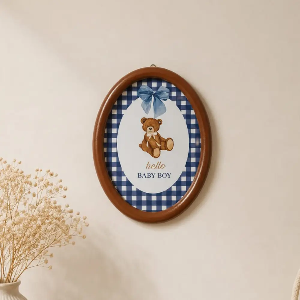 0dd9e436-7242-46aa-8356-7ebd9f4c46bb - Artoza Crafts | Where Craft Becomes Style Oval wooden frame on the wall showcasing a teddy bear print with a blue gingham border and the text 'hello BABY BOY'.
