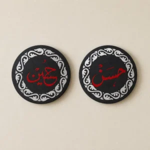 Two black round coasters with a white decorative border and red Arabic calligraphy; the left reads حسين and the right reads حسن.