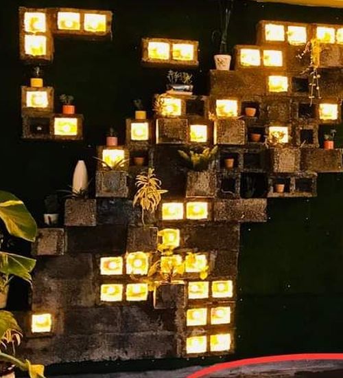 Decorative wall with illuminated yellow square blocks arranged in a staggered pattern, some blocks holding small potted plants.