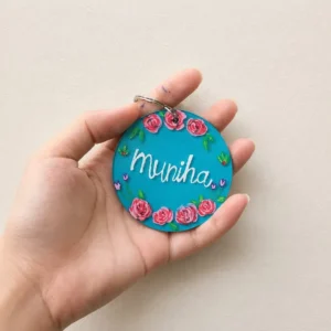Round turquoise keychain with pink rose border and the word 'Minha' in white, held in a hand.