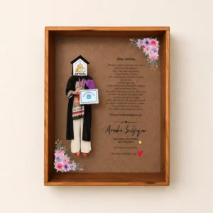Wooden shadow box featuring a graduation keepsake: a figurine in cap and gown holding a certificate, with pink and purple flowers decoration.