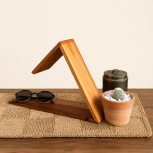 Decorative wooden geometric sculpture on a woven mat, with sunglasses, a small potted cactus, and a dark metal container nearby.