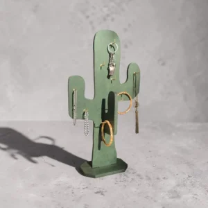 Green cactus-shaped jewelry stand with gold and silver earrings and rings on a gray surface.
