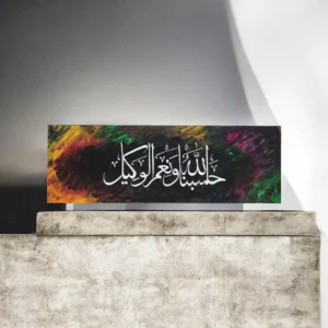 Colorful abstract background with white Arabic calligraphy on a black panel atop a concrete pedestal.