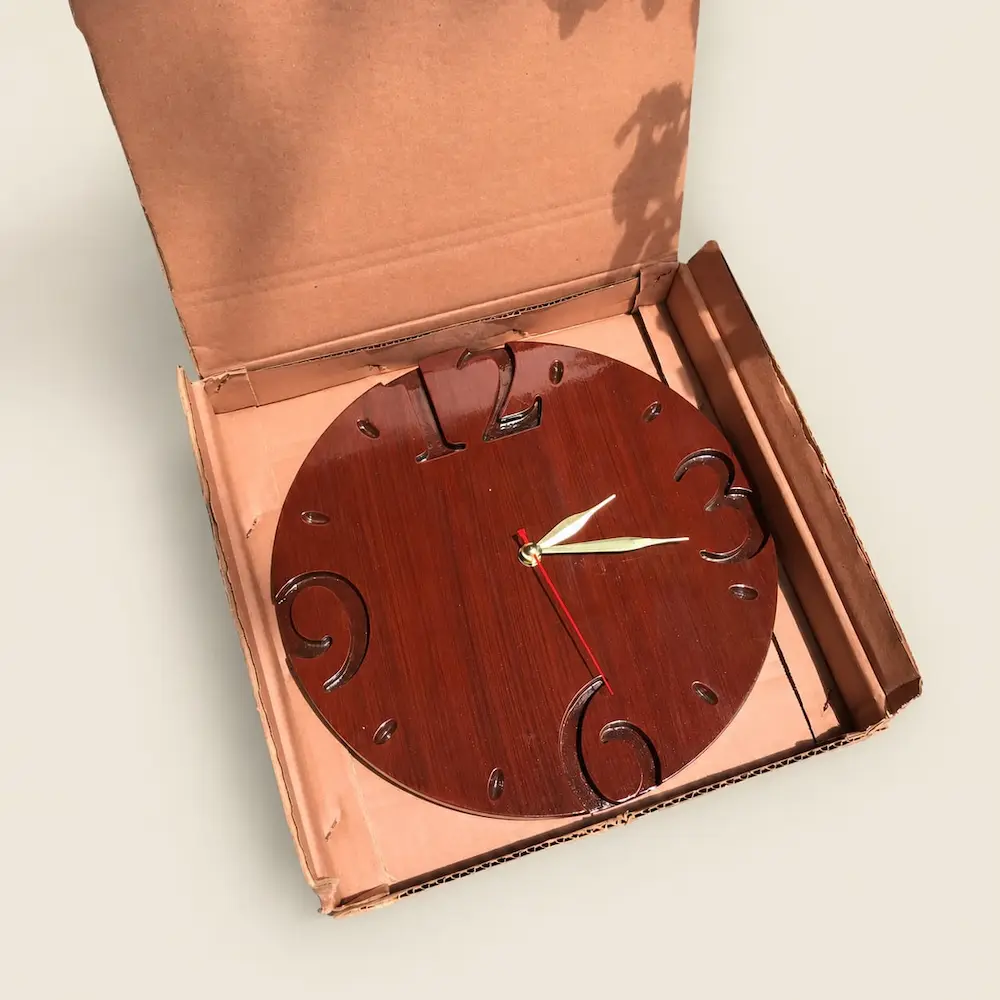 circular clock - Artoza Crafts | Where Craft Becomes Style Round wooden clock with oversized carved numerals sits in a pink inner box inside a brown shipping carton, ready for display or sale.