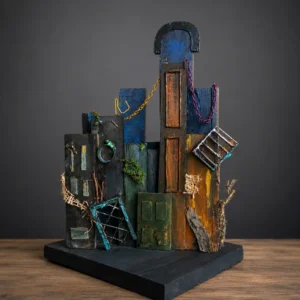 Mixed-media sculpture of a decaying city block with weathered wooden buildings, chains, and broken windows on a black pedestal.