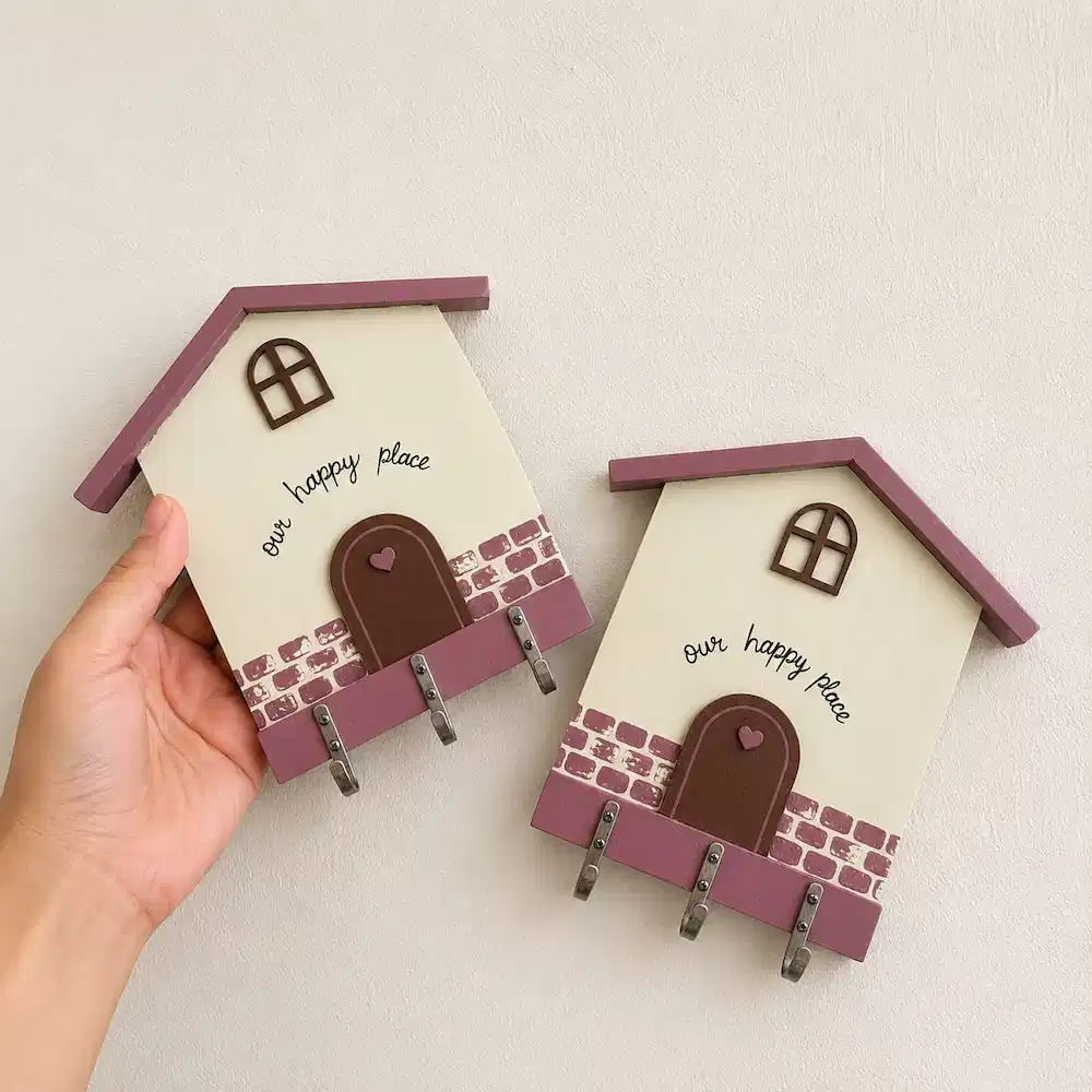 diy keyholders - Artoza Crafts | Where Craft Becomes Style Two decorative wooden houses with pink roofs and four hooks along the bottom; one is held by a hand.
