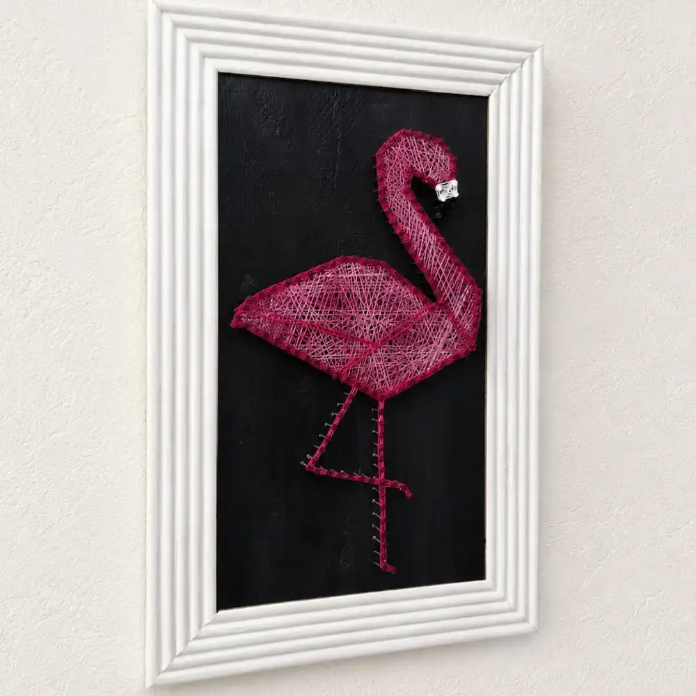 flamings thread art - Artoza Crafts | Where Craft Becomes Style Pink string-art flamingo on a black background, framed in a white decorative frame.