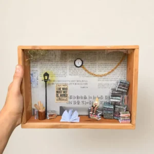 gift for book lovers - Artoza Crafts | Where Craft Becomes Style Handheld wooden shadow box with mini desk scene: lamp post, clock, tiny person reading, books piled on the right, and open notebook on the desk side.