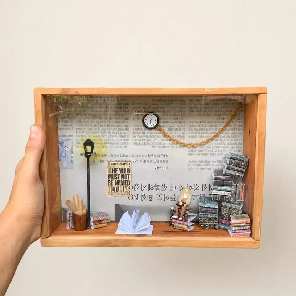 gift for book lovers - Artoza Crafts | Where Craft Becomes Style Handheld wooden shadow box with mini desk scene: lamp post, clock, tiny person reading, books piled on the right, and open notebook on the desk side.