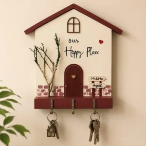 Wooden house-shaped key holder with 'our Happy Place' text, red door, mini brick accent, and three hooks holding keys.
