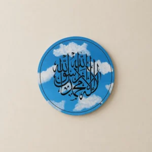 Round blue circular wall art with intricate Arabic calligraphy set against a sky with white clouds, mounted on a beige wall.