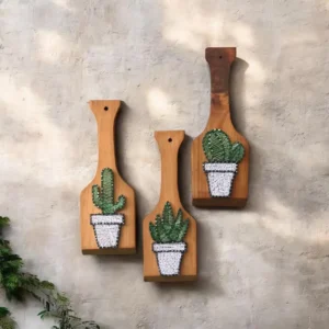 Three wooden cutting boards mounted on a gray wall, each with a crocheted cactus in a pot.|lm:2