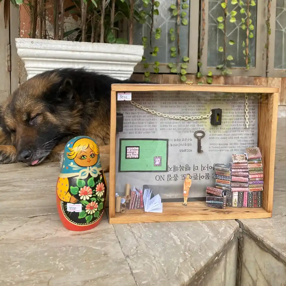liberary theme gifts - Artoza Crafts | Where Craft Becomes Style Sleeping dog beside a wooden display case filled with miniature books, a key, chains and paper crafts.