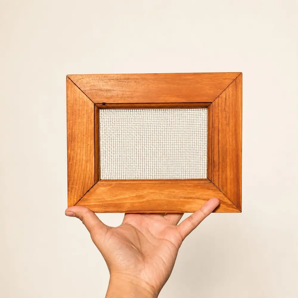mesh frame - Artoza Crafts | Where Craft Becomes Style Hand holding a square wooden frame with a woven mesh screen in the center against a light background.