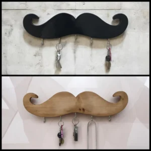 Black mustache-shaped key rack on a concrete wall with keys hanging from its hooks in the top panel.