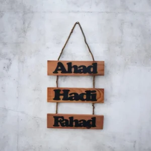 Wooden three-panel wall sign with names Ahad, Hadi, and Fahad hanging by rope on a concrete wall.