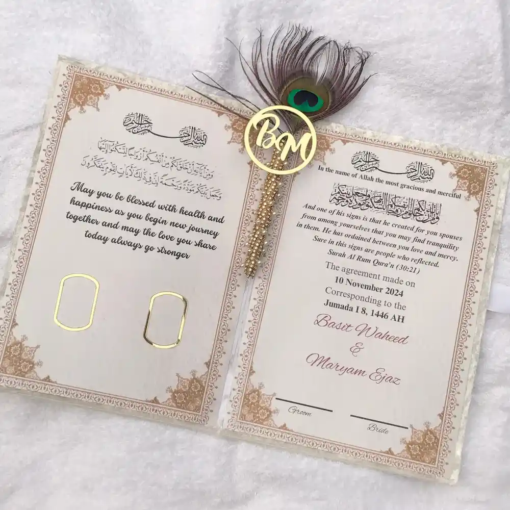 nikah certificate - Artoza Crafts | Where Craft Becomes Style Open wedding invitation with gold floral border, two gold rings, and a peacock feather charm accessory in the corner.