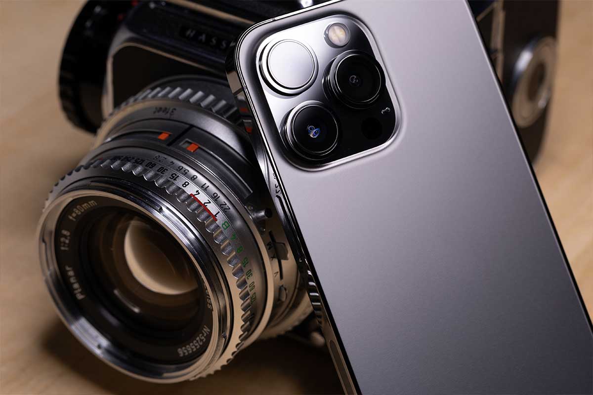 Close-up of a vintage camera lens beside a modern smartphone with a triple-camera setup, illustrating photography gear.
