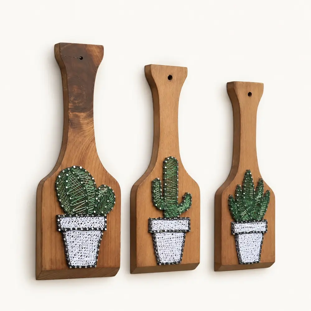 set of 3 cactus string art - Artoza Crafts | Where Craft Becomes Style Three wooden cutting boards of varying sizes with embroidered cactus plant designs in white pots, hung in a row against a light background.