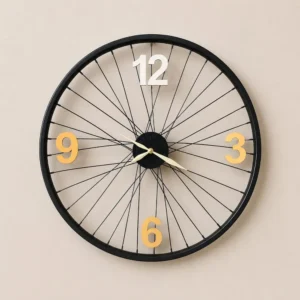 Wall clock with a black bicycle-wheel frame and large gold numbers at 12, 3, 6, and 9 on a beige wall.