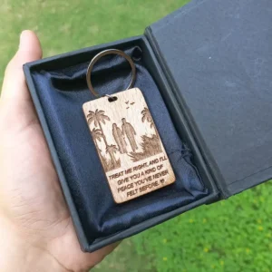 Wooden keychain in a box featuring a couple holding hands under palm trees with a romantic quote engraved on it/saying: 'Treat me right and I'll give you a kind of peace you've never felt before'