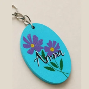 Oval turquoise wooden keychain with purple flowers, green leaves, and the name Anna written in black script.