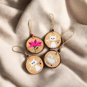 Four round wooden ornaments with hand-painted white cats and a pink flower, hung on twine.
