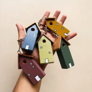 Hand holding a handful of small wooden house-shaped keychains painted in blue, yellow, green, purple, and brown.