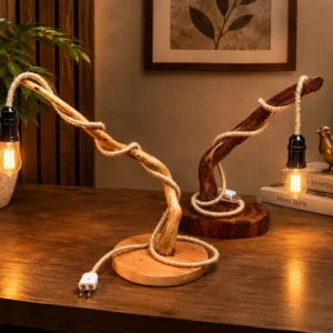 Two curved wooden branch lamps wrapped in rope sit on a dark wood desk, their warm Edison bulbs glowing beside a potted plant and books.