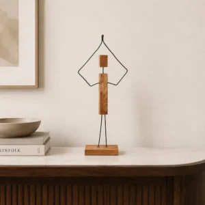 Minimalist wooden sculpture with metal wire arms on a small base, placed on a marble console.