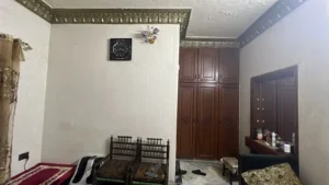 A bedroom with a dark wood wardrobe against the wall, a dresser with a mirror, and a small seating area nearby.