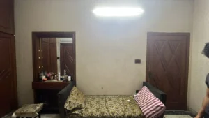 Small bedroom with beige walls, a patterned sofa bed, striped pink pillow, and a dresser with a mirror on the left.