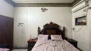 Bedroom with an ornate dark wood bed, floral bedding, and matching nightstands on each side of a white paneled wall. A wall AC unit is mounted on the right.
