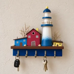 Decorative wooden key rack with a blue and brown scene featuring a lighthouse and small red and blue houses; keys hang from hooks below.